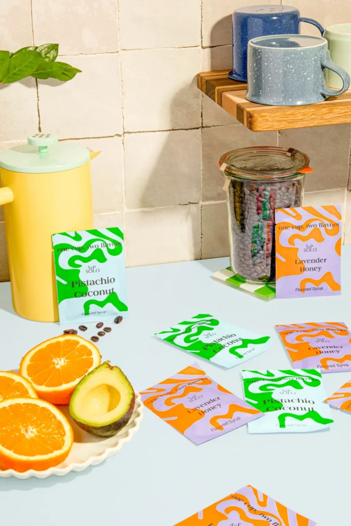 Packets of Sip Solo spread out on a kitchen counter with sliced avocado and orange halves around it.